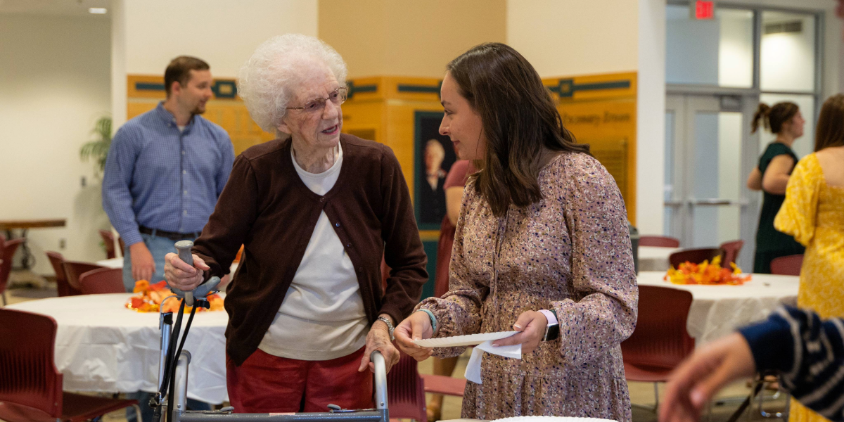 student getting plate of food for older lady at the Servants Day tea party in brown kopel business center