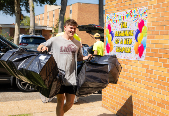 Man helping carry a new students items to their room