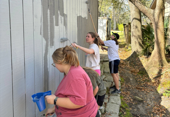 Three FHU students and an FHU alumni painting the side of a house
