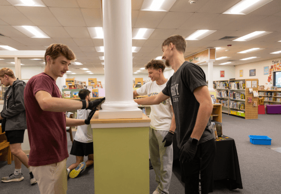 5 male students working on wiping down surfaces inside the chester county library