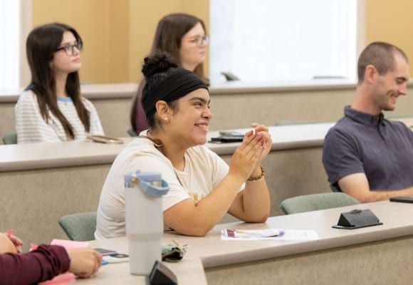 Smiling students sit behind tables in classroom