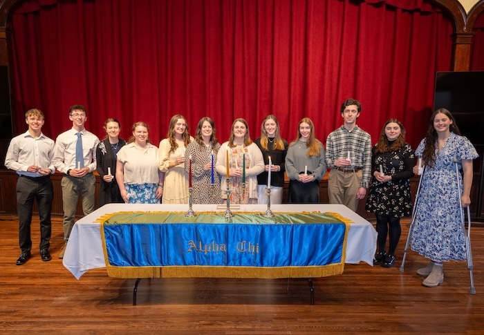 Students holding candles stand behind a table during an Alpha Chi induction ceremony.