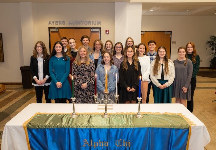 Alpha Chi members standing behind a table with candles