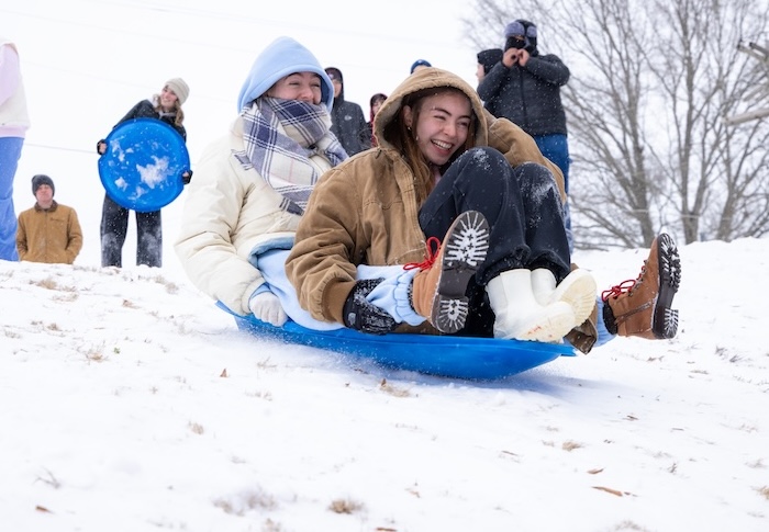 Two female students sled down a hill during a campus snow day