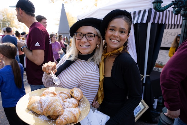 Two Sigma Rho students offer a plate of croissants at tailgating party