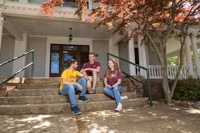 Three students sit on porch of McDaniel House